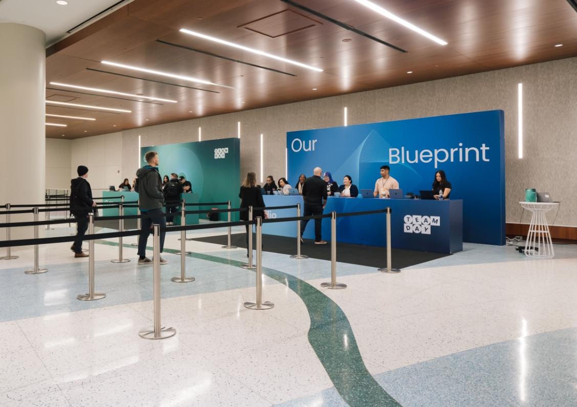 People are gathered at a modern registration desk with a blue "Our Blueprint" backdrop.