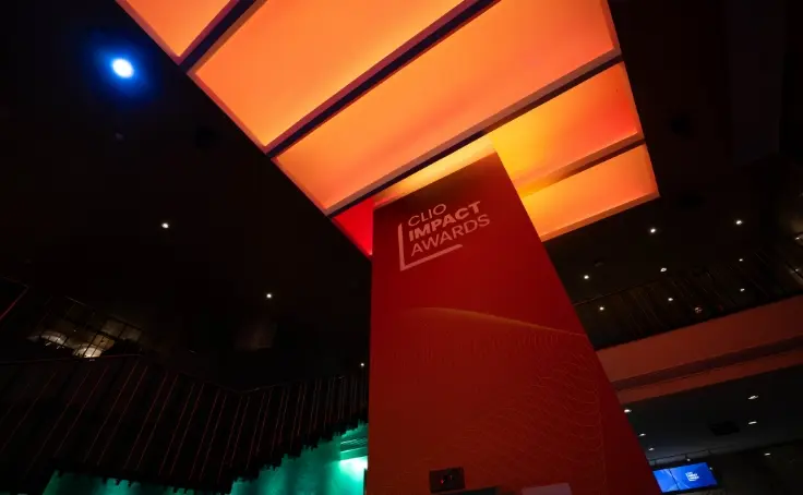 Un espace intérieur illuminé en rouge et orange présentant un panneau pour les Clio Impact Awards.