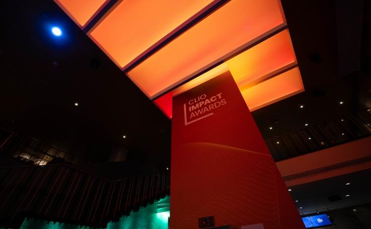 A red and orange illuminated indoor space featuring a sign for the Clio Impact Awards.