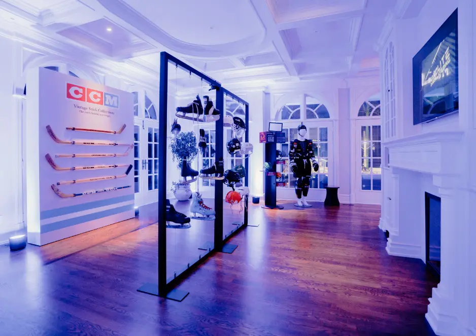 An illuminated room displays vintage CCM hockey equipment, including sticks and gear, with sports memorabilia on display racks.