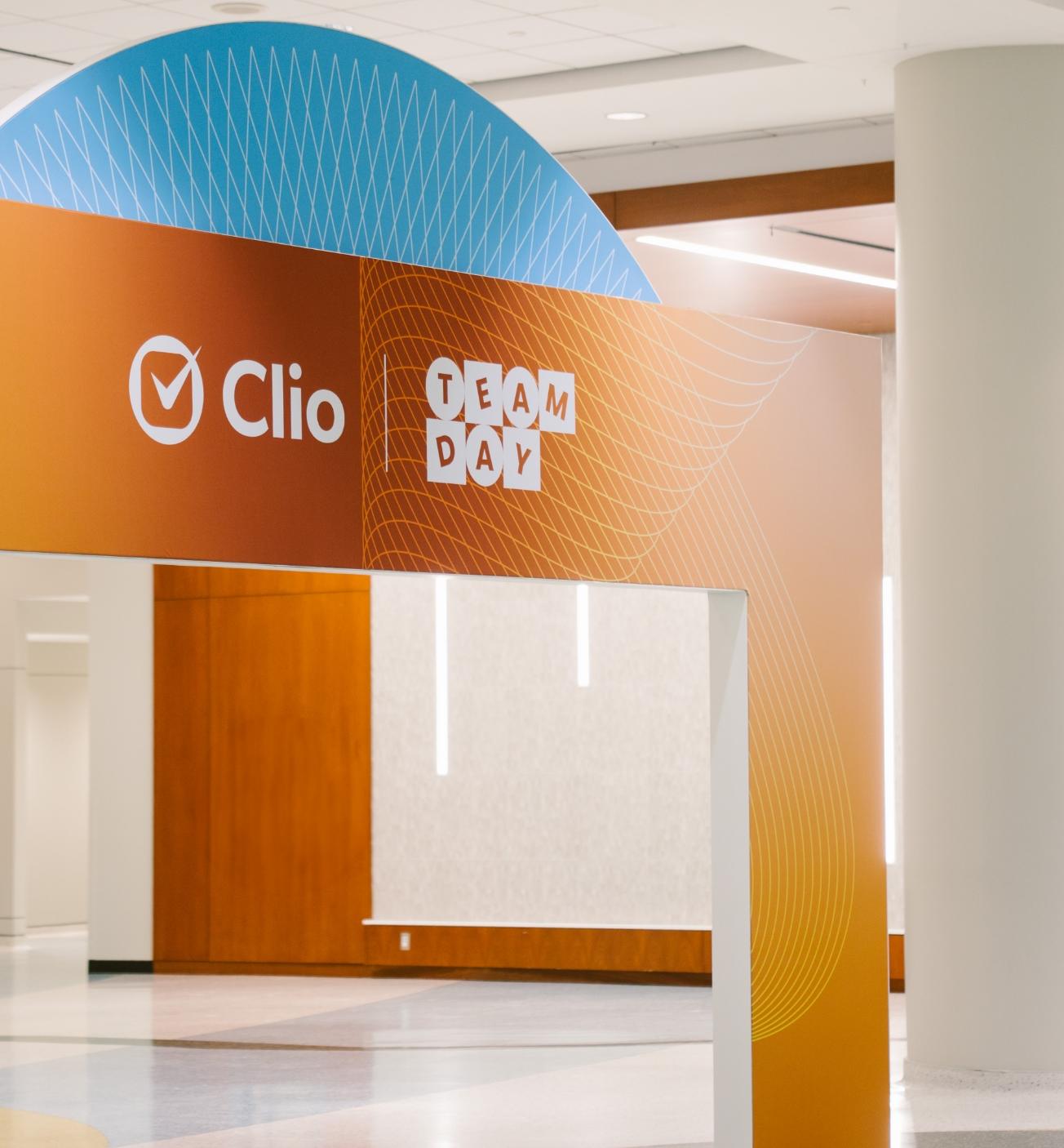 A decorative archway with the words "Clio" and "Team Day" is displayed indoors.